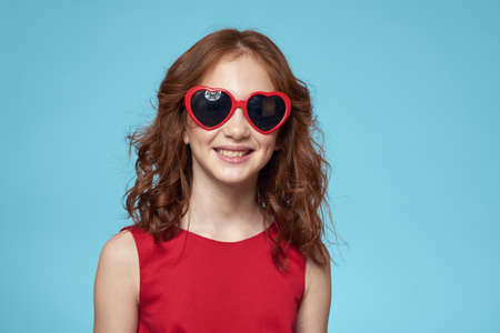 Little girl in sunglasses in the form of hearts red dress curly hair blue backgroundの写真素材