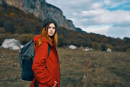 a woman in a red jacket and warm hats walks in a meadow in the mountains in natureの写真素材