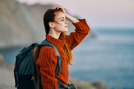 pretty woman in a sweater with a backpack on her back and sea mountains nature fresh air