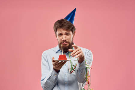 Birthday of a man with a cake and with a candle on a pink backgroundの写真素材