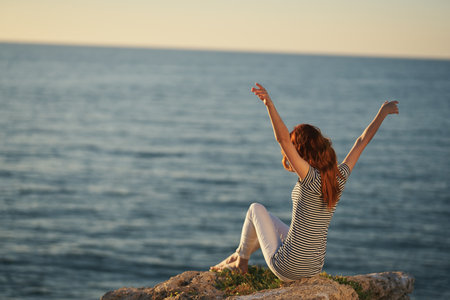 happy woman in a t-shirt and trousers by the sea raised her hands upの写真素材