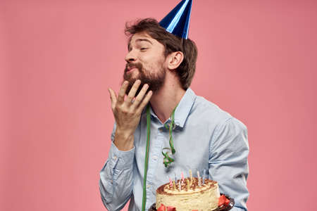 Bearded man with cake tongue on a pink background cropped view and a blue cap on his head
