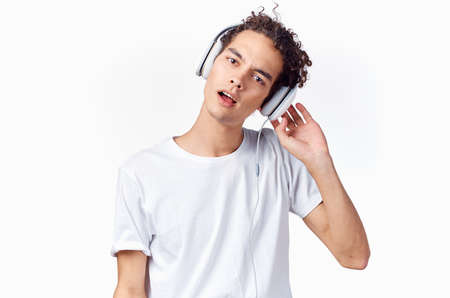 happy curly-haired guy in headphones and in a white t-shirt listens to music and holds his hands near his faceの写真素材