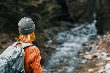 woman near the river in the mountains with a backpack on her shoulders are resting in the autumn...