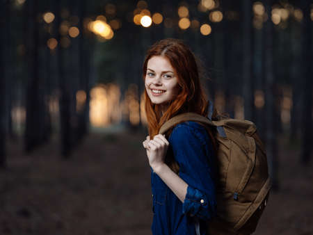 Woman with a backpack and in a blue shirt near the trees in the forest smiling modelの写真素材