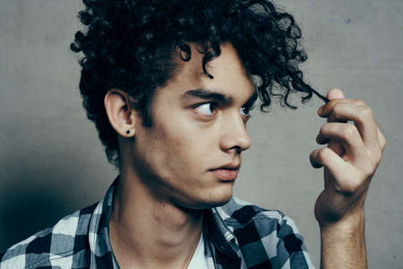man examines his locks of hair and gray background plaid shirt handsome guy modelの写真素材