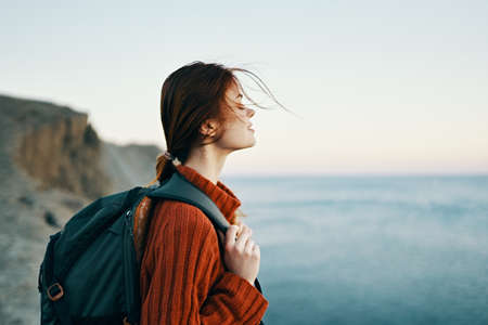 woman tourist with a backpack in a sweater are resting in the mountains near the sea and looking at the skyの写真素材