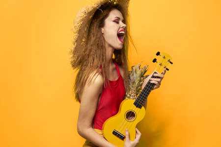 Cheerful woman in red ukulele t-shirt Exotic fruit yellow background lifestyle