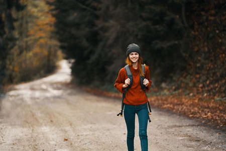 woman with a backpack in full growth walks along the road in the forest in autumnの写真素材