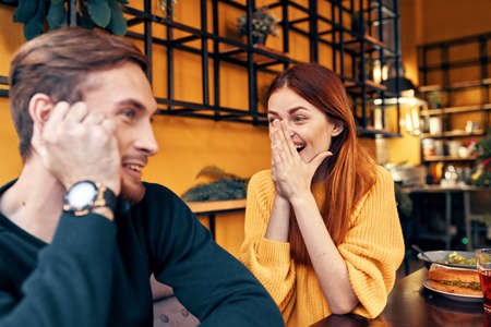 happy woman in a sweater gestures with her hands fun emotions and a man in a sweater sits in a cafeの写真素材