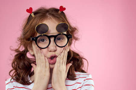 little girl in fashionable glasses and clothespins on her hair emotions pink background heartsの写真素材