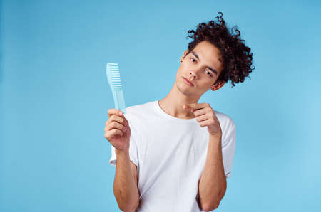 emotional man with a comb in his hand and curly hair in a blue background Copy Space