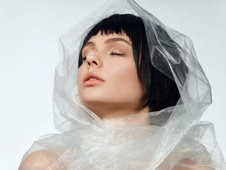 beautiful woman with dark hair makeup closed eyes and transparent cloth on her headの写真素材