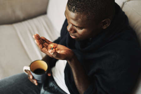 sick man drinking pills Sitting on the couch with a cup in his hand