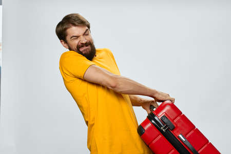 a man in a yellow t-shirt with a heavy suitcase on a light backgroundの写真素材