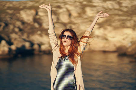 happy woman in a t-shirt holds her hands above her head in the mountains in nature near the river