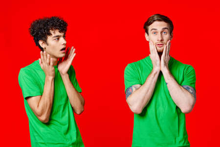 two men holding their heads in green T-shirts on a red backgroundの写真素材