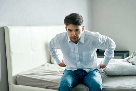 man in shirt and jeans sits on the bed indoors interior lonelinessの写真素材