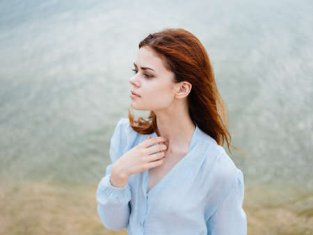 A woman travels on the beach near the sea in a blue shirt with red hair