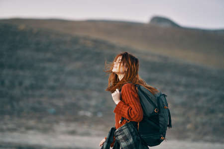 woman in red sweater with backpack looks back on nature in the mountainsの写真素材