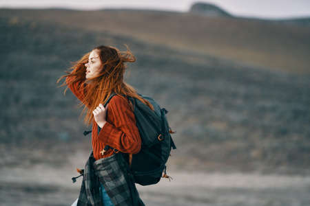 red-haired traveler with a backpack looks back on the nature in the mountainsの写真素材