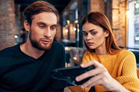 a woman in a sweater with a mobile phone and a guy with a beard are sitting in a restaurant