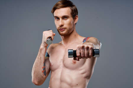 sporty male bodybuilder with pumped up arm muscles and color tattoo dumbbell biceps