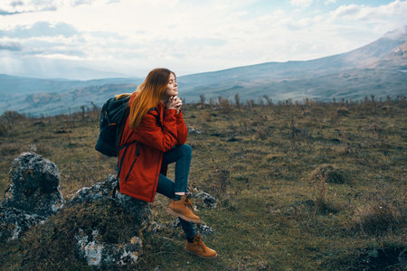 woman traveler in a jacket sits on the Big Stone and looks at the mountains landscapeの写真素材