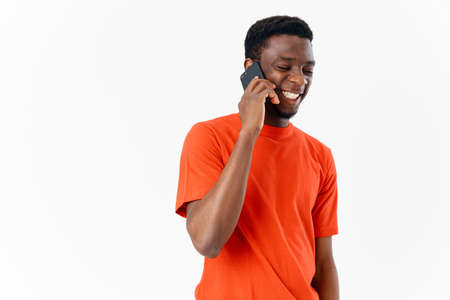 happy guy of african appearance talking on the phone on a light background and an orange t-shirt smile modelの写真素材