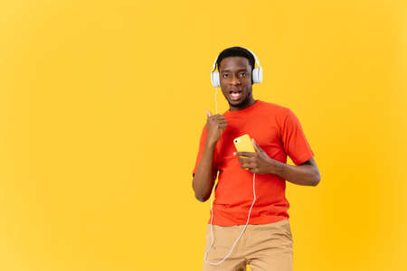 African American with a phone in his hands in headphones listens to music yellow background