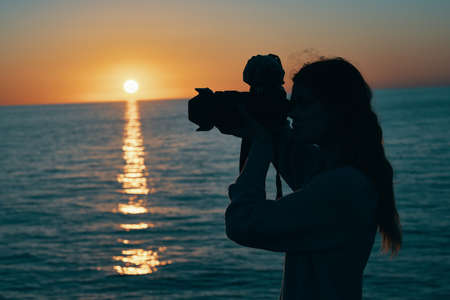 woman photographer with camera at sunset near the sea nature landscapeの写真素材