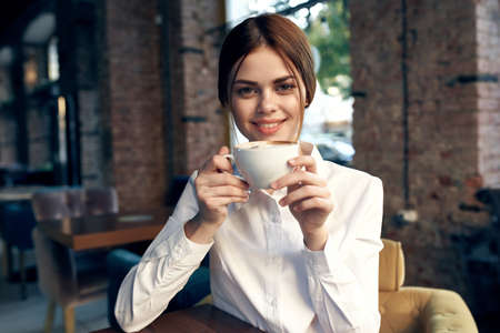 pretty business woman in white shirt sits in a cafe with a cup of coffee