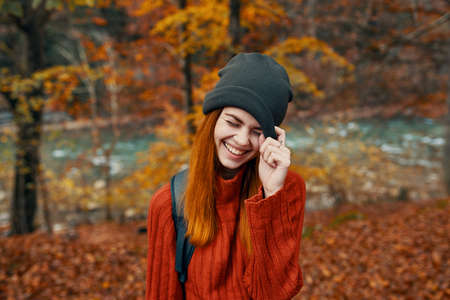 woman in a hat with a backpack and a sweater is resting in the autumn forest near the river in natureの写真素材