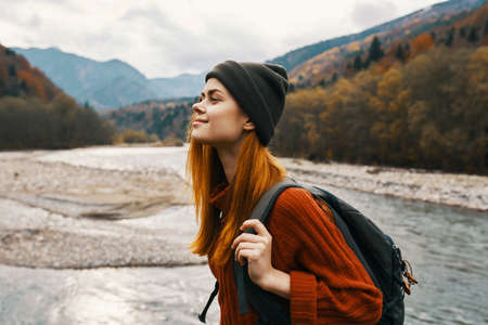 happy traveler with a backpack in a hat and a sweater in the mountains near the riverの写真素材