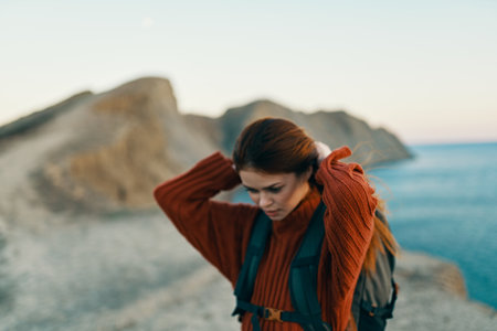 pretty woman in a sweater and jeans with a backpack on her back on nature in the mountains near the seaの写真素材