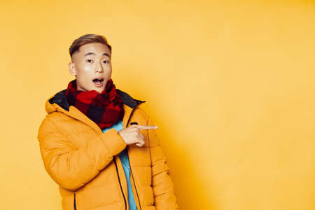 Asian man shows Finger to the side and yellow background warm clothes Copy Space
