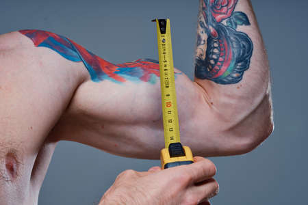 cute athlete with centimeter tape fitness model bodybuilder tattoo on his arm gray backgroundの写真素材