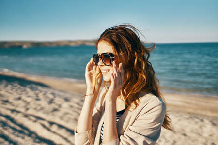 happy red-haired woman in beige jacket and t-shirt on the sand near the sea in the mountainsの写真素材