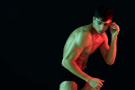 man in shorts posing on a black background with a pumped-up torso biceps fitness