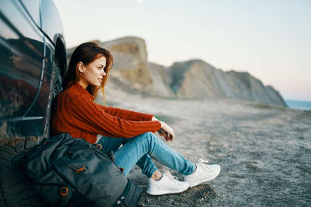 woman in jeans and sneakers sits on the sand near the car in natureの写真素材
