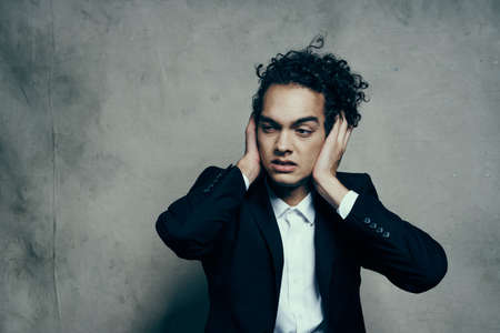 emotional man in classic suit gesturing with his hands indoors with fabric background