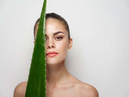 woman touches face with aloe leaf on light background close-up portraitの写真素材