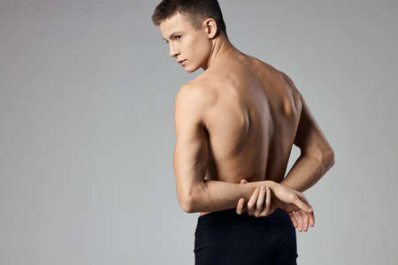 a man with pumped up muscles holds his hands behind his back on a gray background and behind Model...