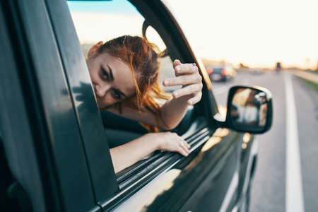 cheerful woman with red hair looks out of the car window on the road in summer vacation relax