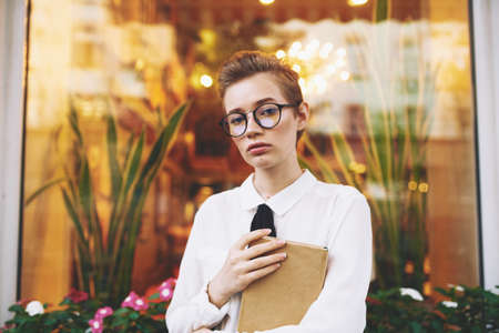 young woman with a book sits in a chair on the sofa in a cafe spring shirt black tie model