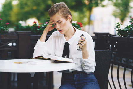 woman reading a book at a table in a restaurant education emotions glasses flowers in the backgroundの写真素材