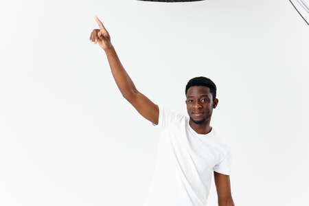 African American in a white t-shirt and beige trousers gesturing with his hands on a light...