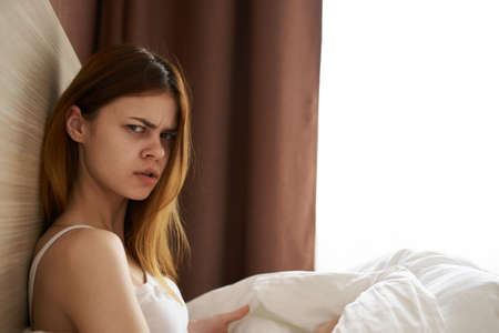 upset woman under blanket bed and open window curtains model side viewの写真素材