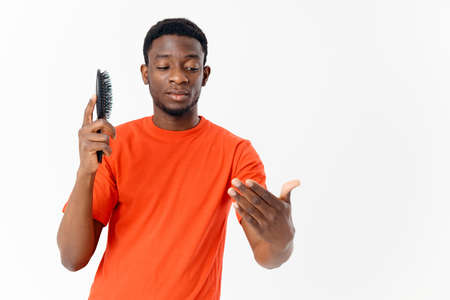 a man of African appearance in an orange T-shirt with a comb in his hands light background