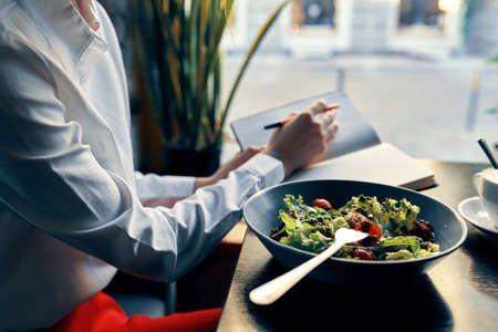 delicious food salad in a plate fork notepad with the inscription and woman in shirt cafe interior